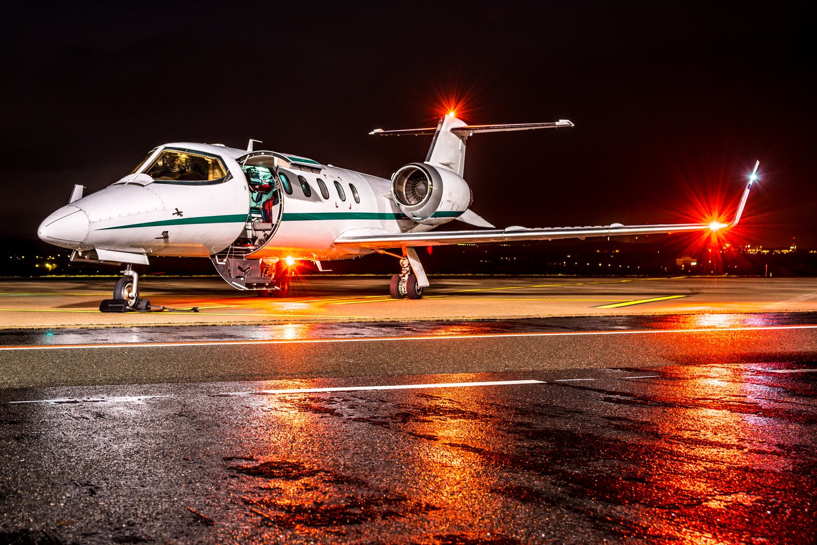 A business jet at night parked on wet apron with position lights illuminated waiting for passengers.